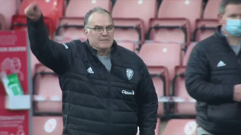 A Man Wearing A Black Jacket And Glasses Is Standing In A Stadium . GIF