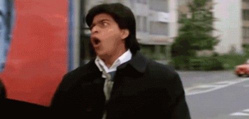 A Man Wearing A Black Jacket And Tie Is Making A Funny Face . GIF