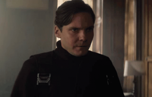 A Man Wearing A Black Jacket With The Letter K On It Looks At The Camera GIF