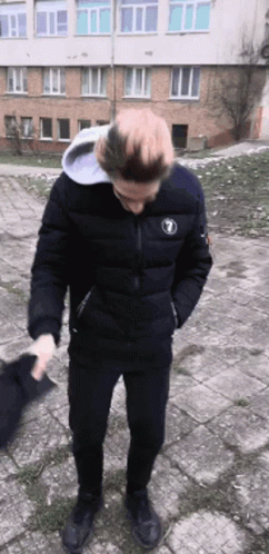 A Man Wearing A Black Jacket With The Number 1 On It Is Standing In Front Of A Building GIF