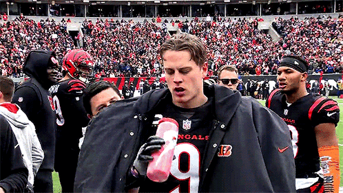 a man wearing a black jacket with the number 9 on it is holding a pink water bottle
