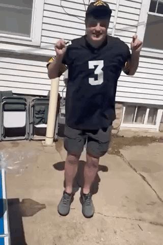 A Man Wearing A Black Jersey With The Number 3 On It Is Standing In Front Of A White House . GIF