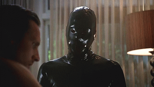 A Man Wearing A Black Latex Mask Looks At Another Man GIF
