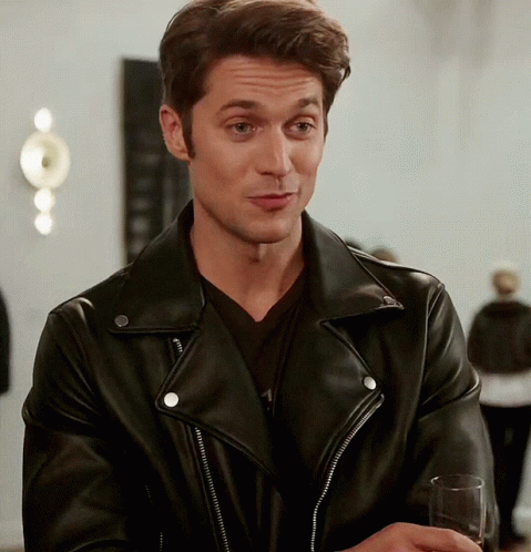 A Man Wearing A Black Leather Jacket Holds A Glass Of Wine GIF