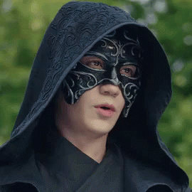 A Man Wearing A Black Mask And A Hood Is Looking At The Camera . GIF