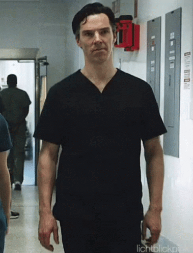 a man wearing a black scrub top is walking down a hallway .