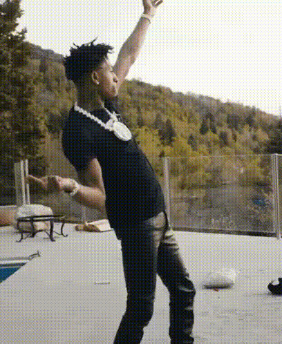 A Man Wearing A Black Shirt And A Necklace Is Dancing On A Patio . GIF