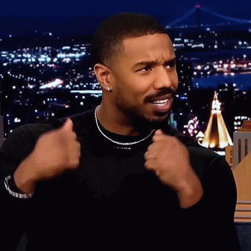A Man Wearing A Black Shirt And A Necklace Is Giving A Thumbs Up Sign GIF