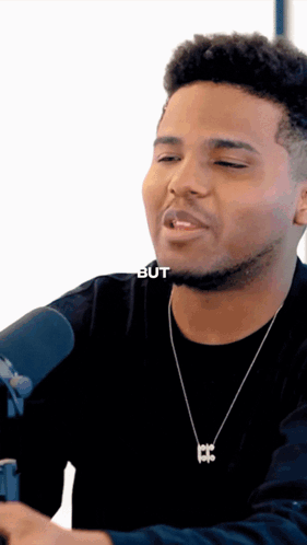 A Man Wearing A Black Shirt And A Necklace With A Letter B On It GIF