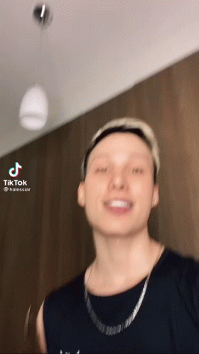 A Man Wearing A Black Shirt And A Silver Chain Is Smiling . GIF
