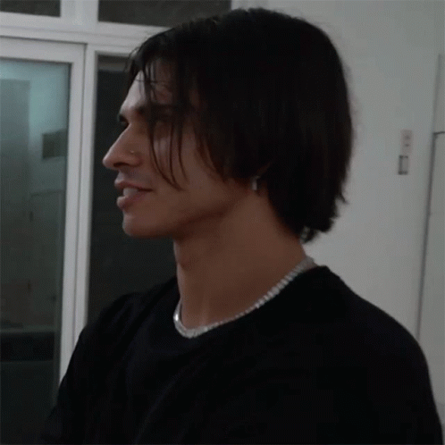 A Man Wearing A Black Shirt And A Silver Necklace Looks To The Side GIF