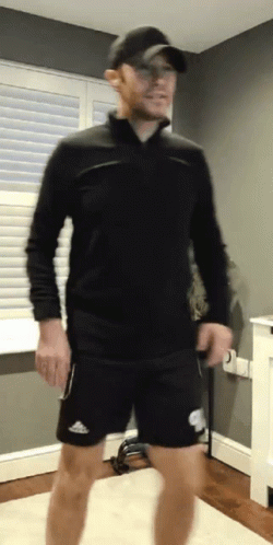 A Man Wearing A Black Shirt And Black Shorts Is Standing In A Room GIF