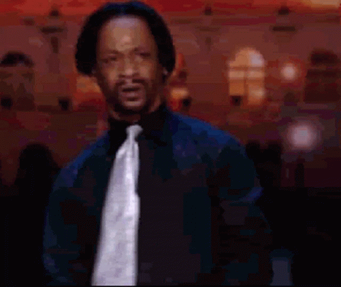 A Man Wearing A Black Shirt And Tie Is Standing In Front Of A Building GIF