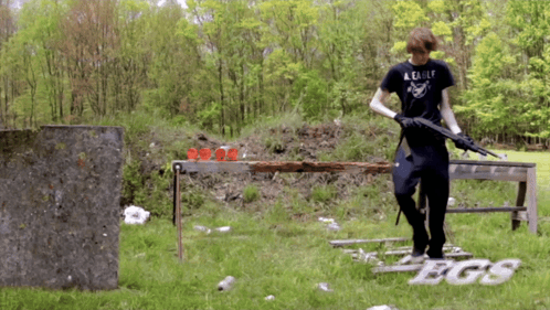 A Man Wearing A Black Shirt That Says A Eagle Holds A Gun GIF