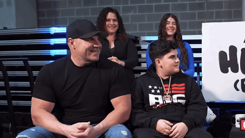 A Man Wearing A Black Shirt That Says Abc Sits Next To Two Other People GIF