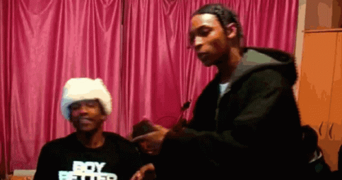 A Man Wearing A Black Shirt That Says Boy Better Is Standing Next To Another Man GIF