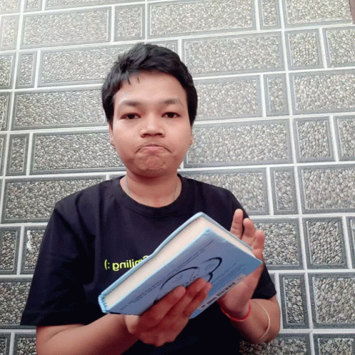 A Man Wearing A Black Shirt That Says ' Brilliance ' On It Holds A Blue Book GIF
