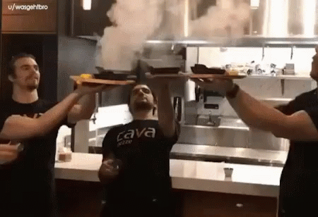 A Man Wearing A Black Shirt That Says Cava On It Holds Up A Tray Of Food GIF