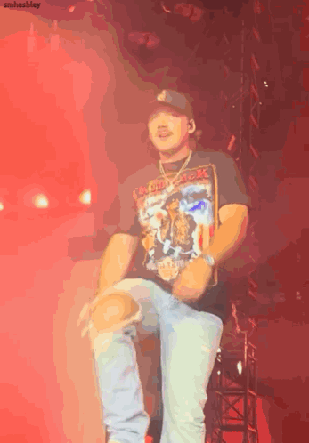 A Man Wearing A Black Shirt That Says Iron Maiden Is Dancing On A Stage GIF