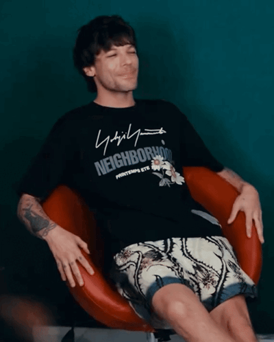 A Man Wearing A Black Shirt That Says Neighborhood Sits In A Chair GIF
