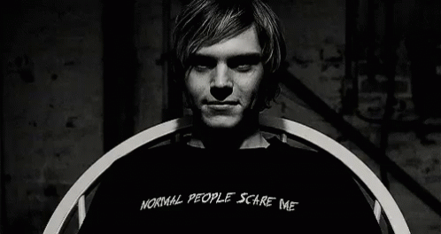 A Man Wearing A Black Shirt That Says `` Normal People Scare Me '' Is Sitting In A Chair . GIF