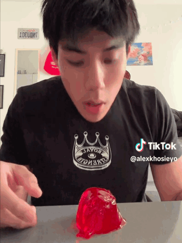 A Man Wearing A Black Shirt With A Crown On It Looks At A Red Jelly GIF