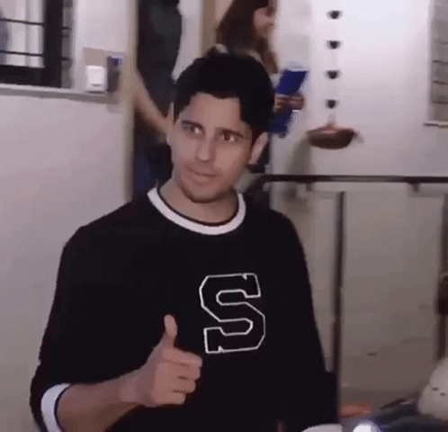 A Man Wearing A Black Shirt With A Letter S On It Is Giving A Thumbs Up . GIF