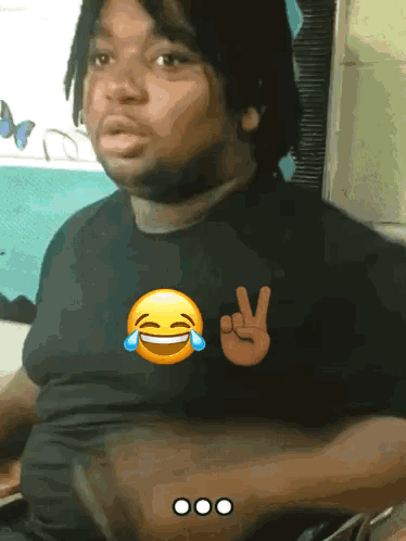 A Man Wearing A Black Shirt With A Peace Sign And A Laughing Face GIF