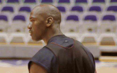 A Man Wearing A Black Shirt With A Red Stripe On The Back Is Standing In Front Of Empty Seats GIF