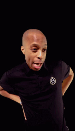 A Man Wearing A Black Shirt With A White Circle With The Letter B On It GIF