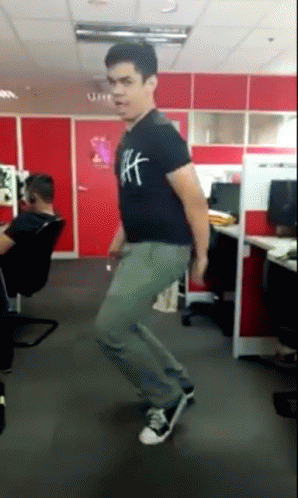 A Man Wearing A Black Shirt With The Letter H On It Is Dancing In An Office GIF