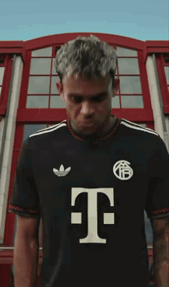 A Man Wearing A Black Shirt With The Letter T On The Front GIF
