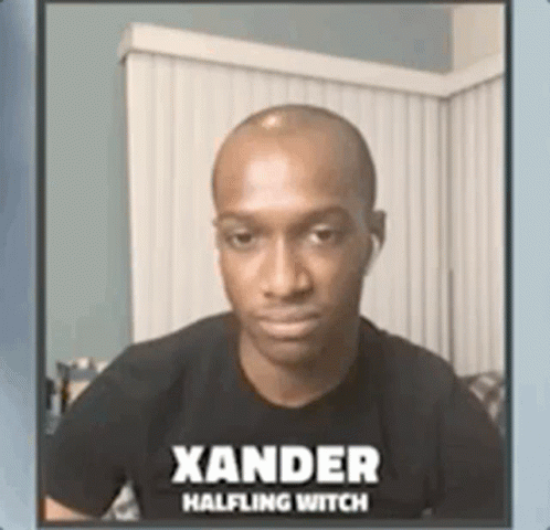 A Man Wearing A Black Shirt With The Name Xander Halfling Witch On It Is Sitting On A Couch . GIF