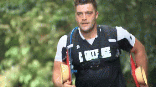 A Man Wearing A Black Shirt With The Word Police On It Is Running Through A Forest . GIF