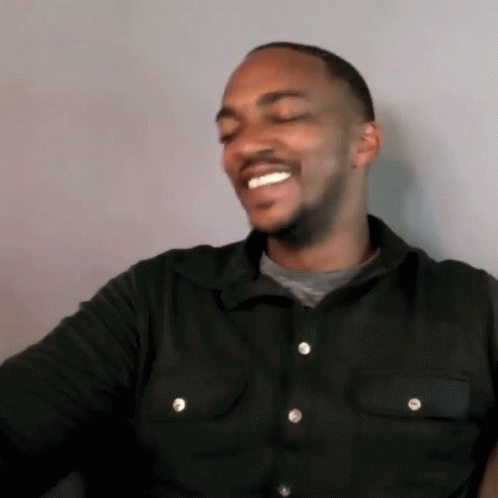 A Man Wearing A Black Shirt With White Buttons Is Smiling GIF