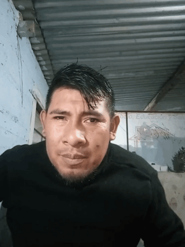 A Man Wearing A Black Sweater Stands In Front Of A Sign That Says Educacion Y Salud GIF