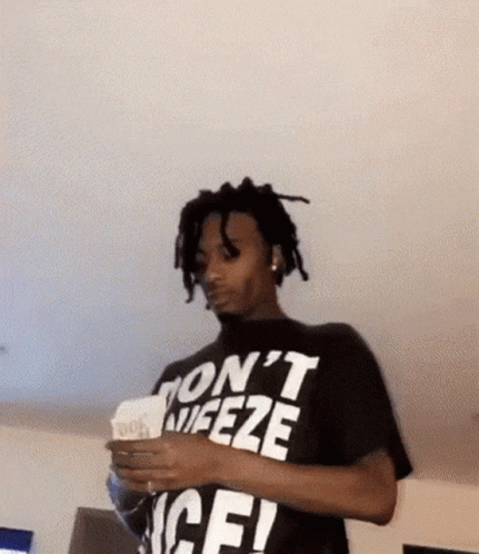 A Man Wearing A Black T-Shirt That Says `` Don 'T Freeze '' Is Holding A Stack Of Money . GIF