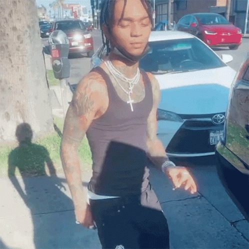 A Man Wearing A Black Tank Top Is Standing In Front Of A White Toyota GIF