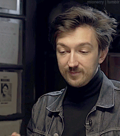 A Man Wearing A Black Turtleneck And A Denim Jacket Is Looking At Something GIF