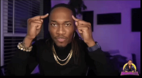 A Man Wearing A Black Turtleneck And Gold Chains Looks At The Camera GIF