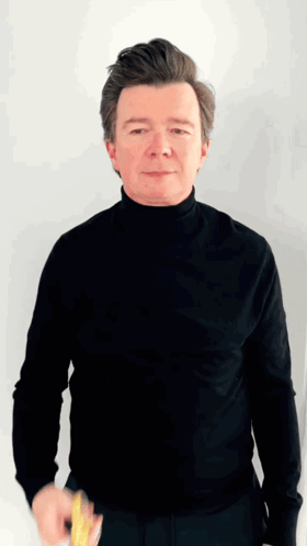 A Man Wearing A Black Turtleneck Is Holding A Yellow Object GIF