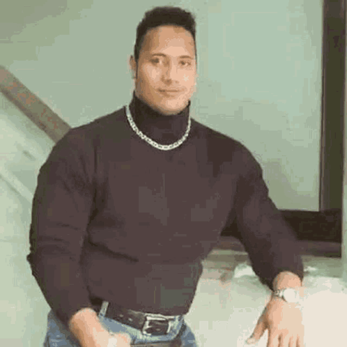 A Man Wearing A Black Turtleneck Sweater And A Chain Around His Neck Is Standing In Front Of A Mirror . GIF