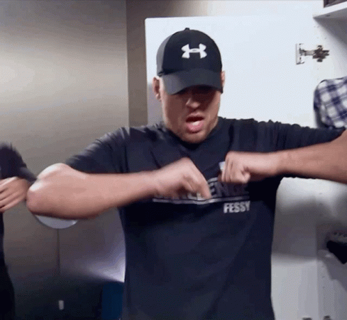 A Man Wearing A Black Under Armour Hat And A Black Shirt That Says Fessy GIF