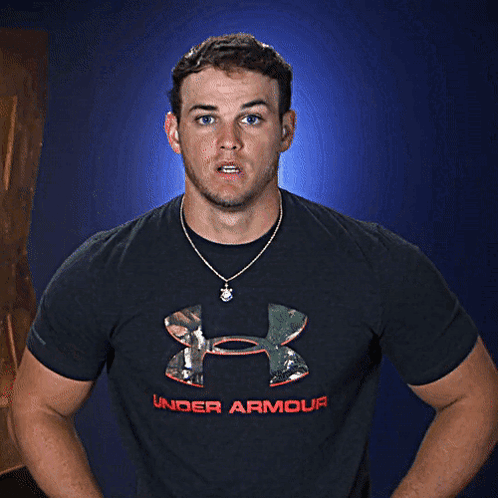 A Man Wearing A Black Under Armour Shirt Stands In Front Of A Blue Background GIF