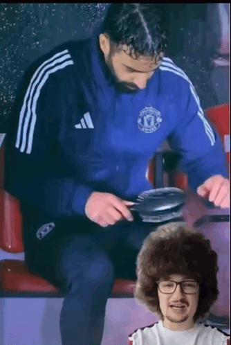A Man Wearing A Blue Adidas Jacket Is Sitting Next To Another Man GIF