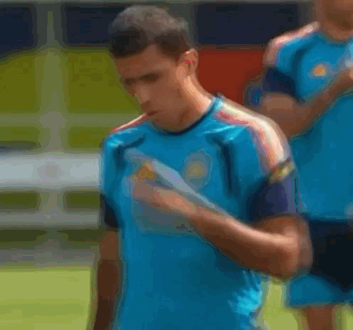 A Man Wearing A Blue Adidas Shirt Is Covering His Mouth With His Hand . GIF
