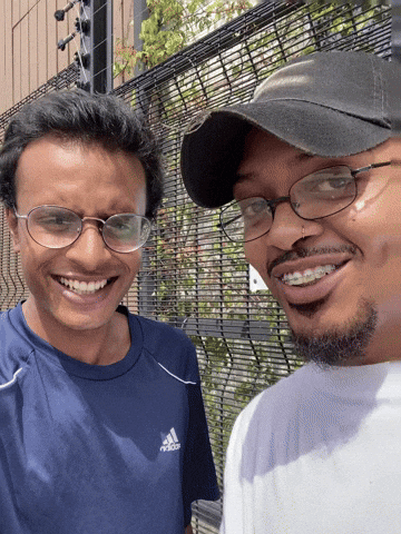 A Man Wearing A Blue Adidas Shirt Smiles Next To Another Man Wearing Glasses GIF