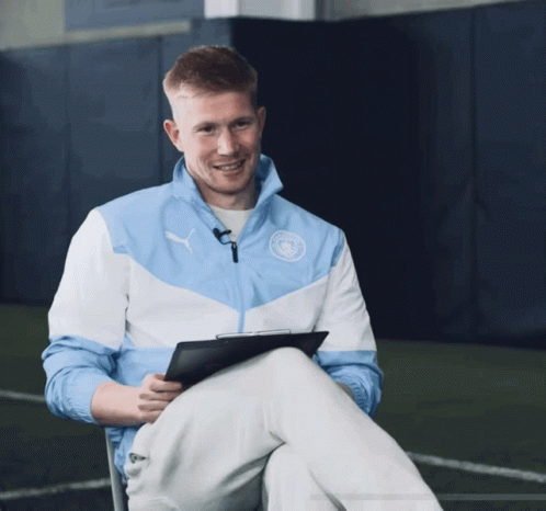 A Man Wearing A Blue And White Puma Jacket Sits With His Legs Crossed GIF