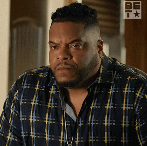 A Man Wearing A Blue And Yellow Plaid Shirt Is Standing In Front Of A Be T Logo GIF