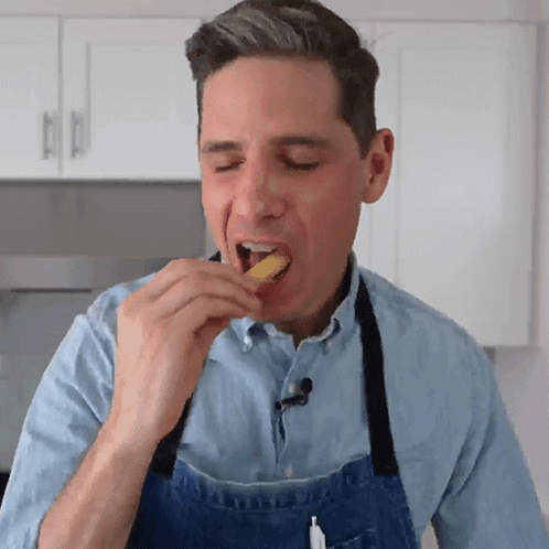 A Man Wearing A Blue Apron Eating A Piece Of Food GIF